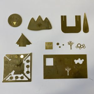a variety of shapes laser cut in brass including trees, mountains, ships and patterns