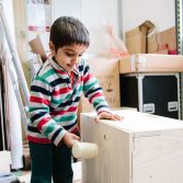 A young boy in a stripey shirt taps a box with a wooden mallet