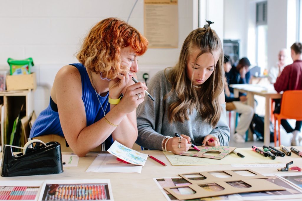 Two people holding markers working on a laser cut piece of cardboard